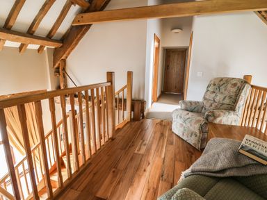 An upstairs hallway with wooden flooring a wooden railing a floral armchair and a doorway at Maes Y Berllan Barn in Gilwern