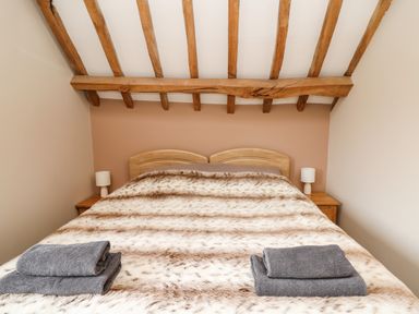 A bedroom with a double bed covered with a fur-like blanket and two folded towels on it at Maes Y Berllan Barn in Gilwern
