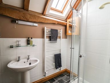 A bathroom with a sink a glass shelf two towels on a radiator and a shower at Maes Y Berllan Barn in Gilwern