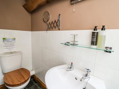 A bathroom with a toilet with wooden seat and a sink with two taps at Maes Y Berllan Barn in Gilwern
