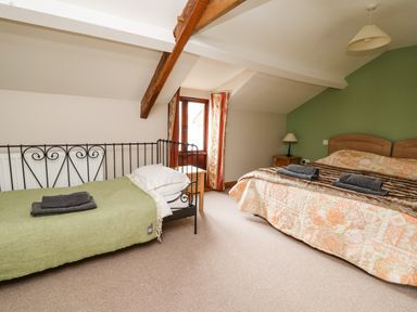 A bedroom with two beds a green wall wooden beams and bedside tables at Maes Y Berllan Barn in Gilwern