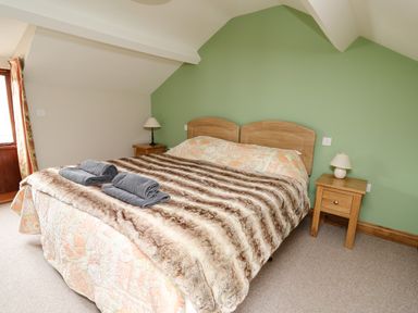 A bedroom with a double bed covered with a patterned quilt and a fur blanket with towels on the bed with two bedside tables with lamps and a green wall at Maes Y Berllan Barn in Gilwern