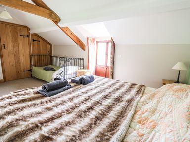 A bedroom with two beds wooden ceiling beams and a small wooden door at Maes Y Berllan Barn in Gilwern