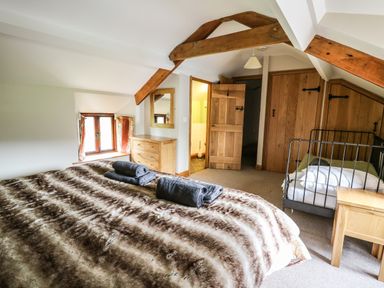 A bedroom with a large bed covered in a striped blanket and a smaller bed with white bedding wooden furniture beams on the ceiling and an open door leading to a bathroom at Maes Y Berllan Barn in Gilwern