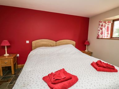 A bedroom with a double bed two wooden bedside tables with lamps and a window with red patterned curtains at Maes Y Berllan Barn in Gilwern