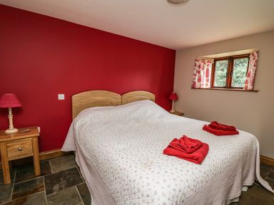 A bedroom with a double bed covered with a white quilt and red towels on the bed two wooden side tables with red lamps and a small window with floral curtains at Maes Y Berllan Barn in Gilwern