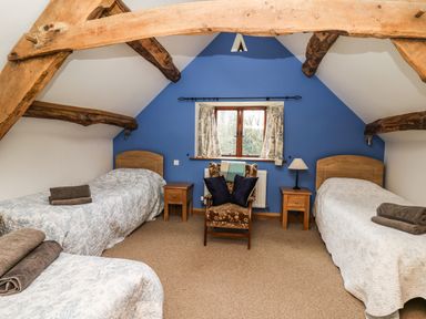 A bedroom with three single beds a wooden armchair and two wooden bedside tables with a lamp at Maes Y Berllan Barn in Gilwern