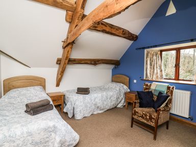 A bedroom with two single beds wooden nightstands a patterned armchair and exposed wooden beams at Maes Y Berllan Barn in Gilwern