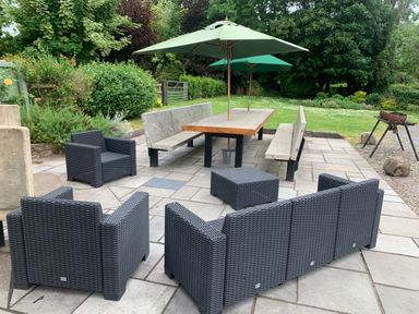 An outdoor patio with wicker chairs and a table with benches and umbrellas at Maes Y Berllan Barn in Gilwern