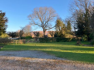 A grassy garden with a metal gate and trees in the background at Maes Y Berllan Barn in Gilwern