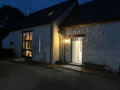 A lit entrance door and windows of a white stone building at night at Maes Y Berllan Barn in Gilwern