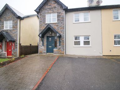 A front view of a stone and plaster house with a blue door and driveway at Pebble Lodge in Kenmare County Kerry