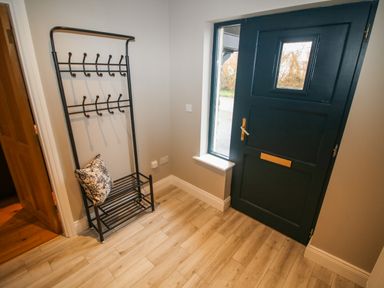 An entryway with a black coat rack with hooks and a cushion near a dark blue front door with a window at Pebble Lodge in Kenmare County Kerry