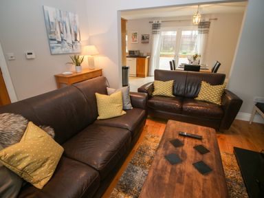 A living room with two brown leather sofas and a wooden coffee table with coasters and remote at Pebble Lodge in Kenmare County Kerry