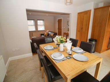A dining area with a wooden table set with dishes and flowers with a living room with sofas in the background at Pebble Lodge in Kenmare County Kerry