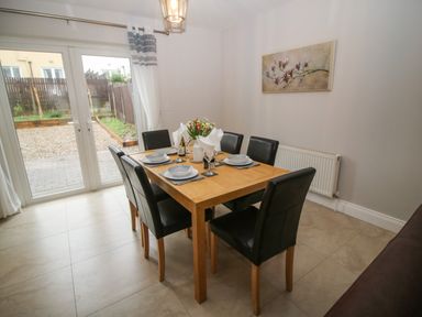 A dining room with a wooden table and six black chairs set with plates and napkins at Pebble Lodge in Kenmare County Kerry