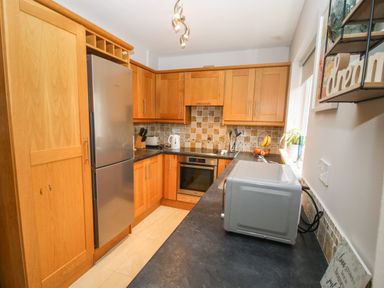 A kitchen with wooden cabinets a stainless steel refrigerator an oven a microwave on the counter and a window with plants at Pebble Lodge in Kenmare County Kerry