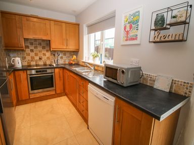 A kitchen with wooden cabinets a black countertop a microwave a dishwasher a sink and a window at Pebble Lodge in Kenmare County Kerry