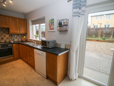 A kitchen with wooden cabinets black countertops a dishwasher microwave and a sliding glass door at Pebble Lodge in Kenmare County Kerry