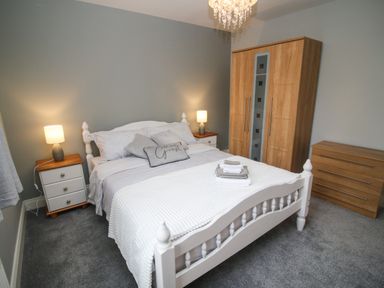 A bedroom with a white bed and bedside tables with lamps a wooden wardrobe and chest of drawers at Pebble Lodge in Kenmare County Kerry