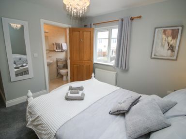 A bedroom with a bed pillows folded towels a window wooden door leading to a bathroom and a wall mirror at Pebble Lodge in Kenmare County Kerry