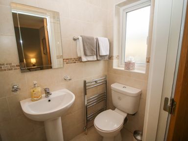 A bathroom with a sink a mirror towels a heated towel rack a toilet and a window at Pebble Lodge in Kenmare County Kerry