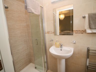 A bathroom with a shower enclosure a pedestal sink a mirror and towels hanging on the wall at Pebble Lodge in Kenmare County Kerry