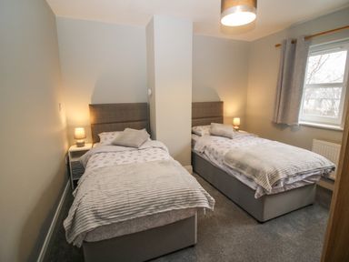A bedroom with two single beds separated by a chimney breast each bed has a bedside table with a lamp and there is a window with curtains at Pebble Lodge in Kenmare County Kerry