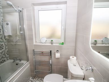 A bathroom with a bathtub shower combo a toilet a towel rack and a window with small plants and a rubber duck on the sill at Pebble Lodge in Kenmare County Kerry