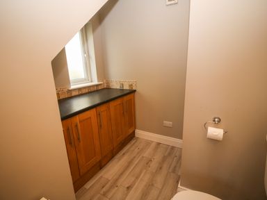 A bathroom with wooden cabinets a counter a window and a toilet paper holder at Pebble Lodge in Kenmare County Kerry