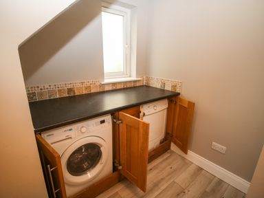 A laundry room with a washing machine and a dryer under a black countertop and a window above at Pebble Lodge in Kenmare County Kerry