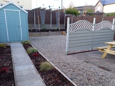 A backyard with a blue shed a stone pathway gravel ground wooden fence and a picnic table at Pebble Lodge in Kenmare County Kerry