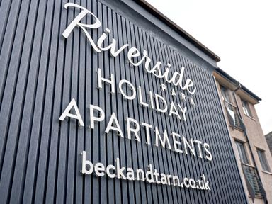 A sign on a building reading Riverside Park Holiday Apartments and beckandtarn.co.uk at Riverside Park in Keswick