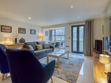 A living room with two blue chairs a gray sofa a wooden coffee table a dining table with chairs and a TV on a wooden stand at Riverside Park 2 in Keswick