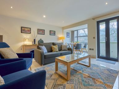 A living room with blue armchairs gray sofa wooden coffee table and dining area by a window at Riverside Park 2 in Keswick