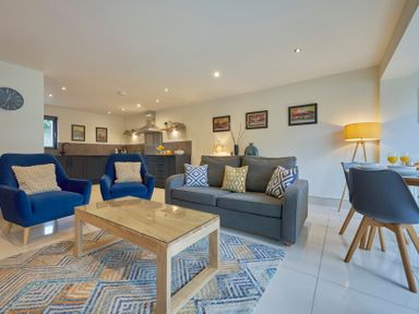 A living room with blue armchairs a gray sofa a wooden coffee table and a kitchen in the background at Riverside Park 2 in Keswick