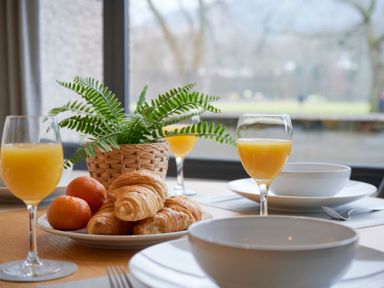 A dining table with croissants tangerines orange juice glasses and a potted plant at Riverside Park 2 in Keswick