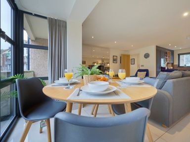 A dining table with plates cups and glasses of orange juice in a living area with large windows at Riverside Park 2 in Keswick