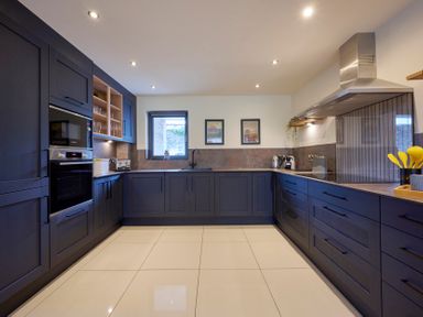 A kitchen with dark cabinets white tiled floor framed pictures on the wall and a stainless steel extractor fan at Riverside Park 2 in Keswick