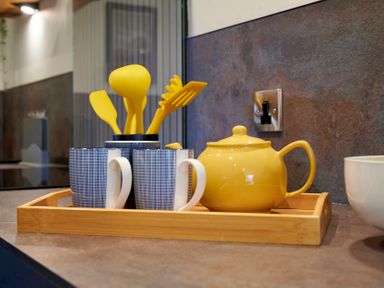 A kitchen countertop with a wooden tray holding a yellow teapot blue and white mugs and yellow kitchen utensils at Riverside Park 2 in Keswick