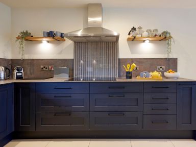 A kitchen with dark blue cabinets stainless steel hood and wooden shelves with cups and jars at Riverside Park 2 in Keswick