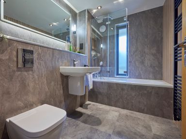 A bathroom with a toilet sink bathtub glass shower panel and a window at Riverside Park 2 in Keswick