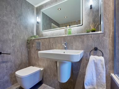 A bathroom with a wall-mounted toilet and a pedestal sink under a large mirror at Riverside Park 2 Keswick