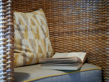 A wicker chair with a patterned cushion and an open book on a grey seat at Riverside Park 2 in Keswick