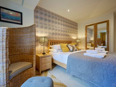 A bedroom with a bed with pillows and folded towels bedside tables with lamps a wicker chair and mirrored closet doors at Riverside Park 2 in Keswick