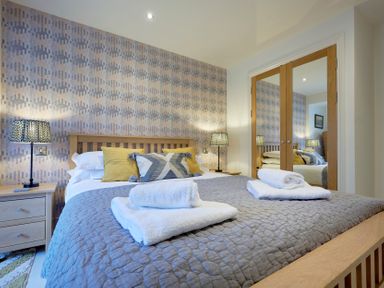 A bedroom with a wooden bed with pillows and folded towels on it two bedside tables with lamps and mirrored closet doors at Riverside Park 2 in Keswick