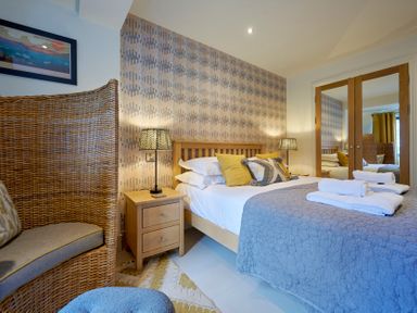 A bedroom with a double bed bedside tables a wicker chair and a mirrored wardrobe at Riverside Park 2 in Keswick