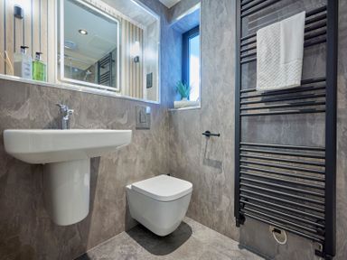 A bathroom with a sink a wall-mounted toilet a towel radiator with a towel and a small window with a plant at Riverside Park 2 in Keswick