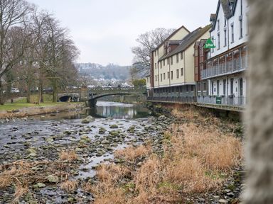 A river with rocks and dry grass next to buildings and a bridge in a town Riverside Park 2 in Keswick