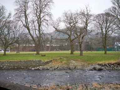 A river in front of a grassy park with leafless trees and a playground at Riverside Park 2 in Keswick